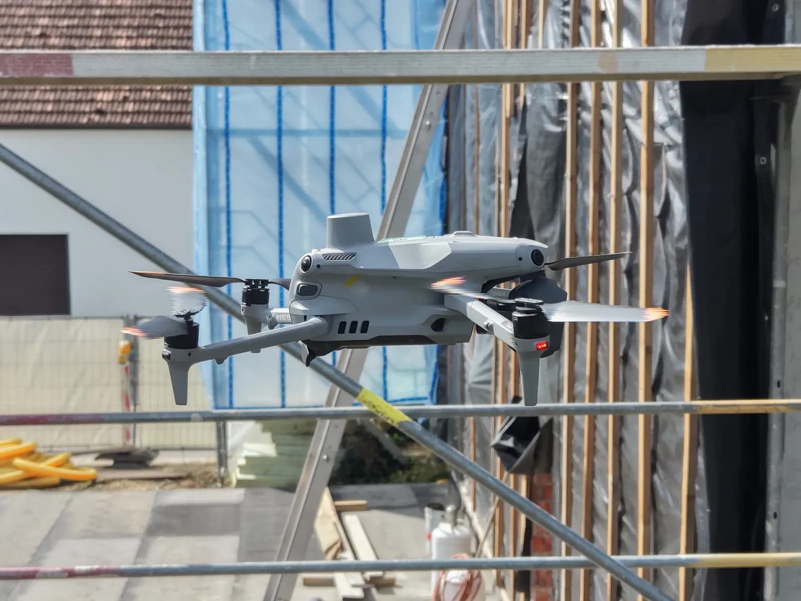 Drohne DJI Matrice 4 fliegt bei der Gebäudevermessung am Gerüst einer Baustelle entlang — 3D-Vermessung aus der Luft mit Photogrammetrie